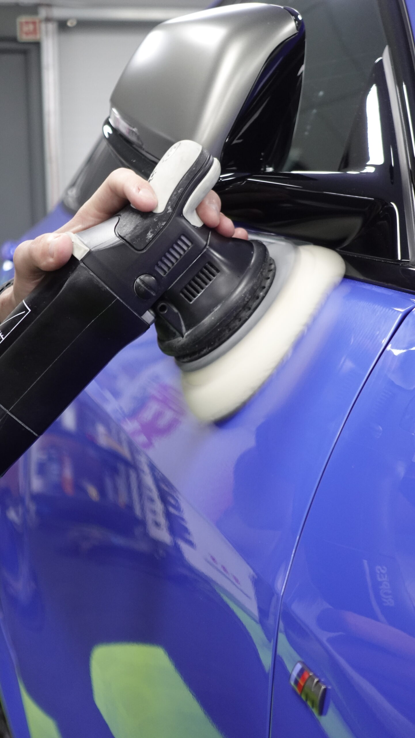 A technician using a dual-action polisher on the blue paint of a car.