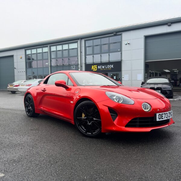 A red Alpine A110 sports car parked outside "New Look Detailing" with a modern detailing facility in the background.